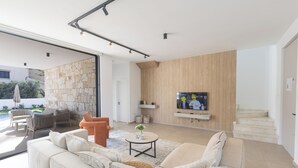 A modern living room with a sofa, chairs, a coffee table, and a TV mounted on a wooden wall. - Ayia Napa Orea Villa OR6 (Ayia Napa)