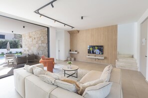 Ein modernes Wohnzimmer mit einer Couch, Sesseln, einem Couchtisch und einem an einer Holzwand montierten Fernseher.