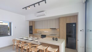 A modern kitchen with a central island, wooden chairs, and built-in appliances. - Ayia Napa Orea Villa OR6 (Ayia Napa)