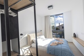 Ein modernes Schlafzimmer mit Bett, einem kleinen Tisch, einem Fenster mit Vorhängen und Blick ins Freie.