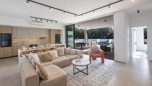 A modern kitchen with a dining area, a living room with a sofa and coffee table, and a sliding glass door leading to an outdoor patio. - Ayia Napa Orea Villa OR6 (Ayia Napa)