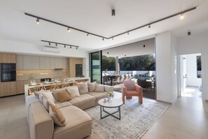 Eine moderne Küche mit Essbereich, ein Wohnzimmer mit Sofa und Couchtisch sowie eine Glastür zum Außenbereich.
