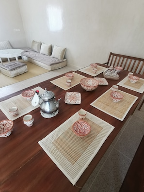 A dining table set with patterned tableware, a silver teapot, and placemats.