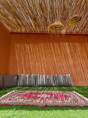 A room with a patterned rug, grey cushions, and a textured ceiling.