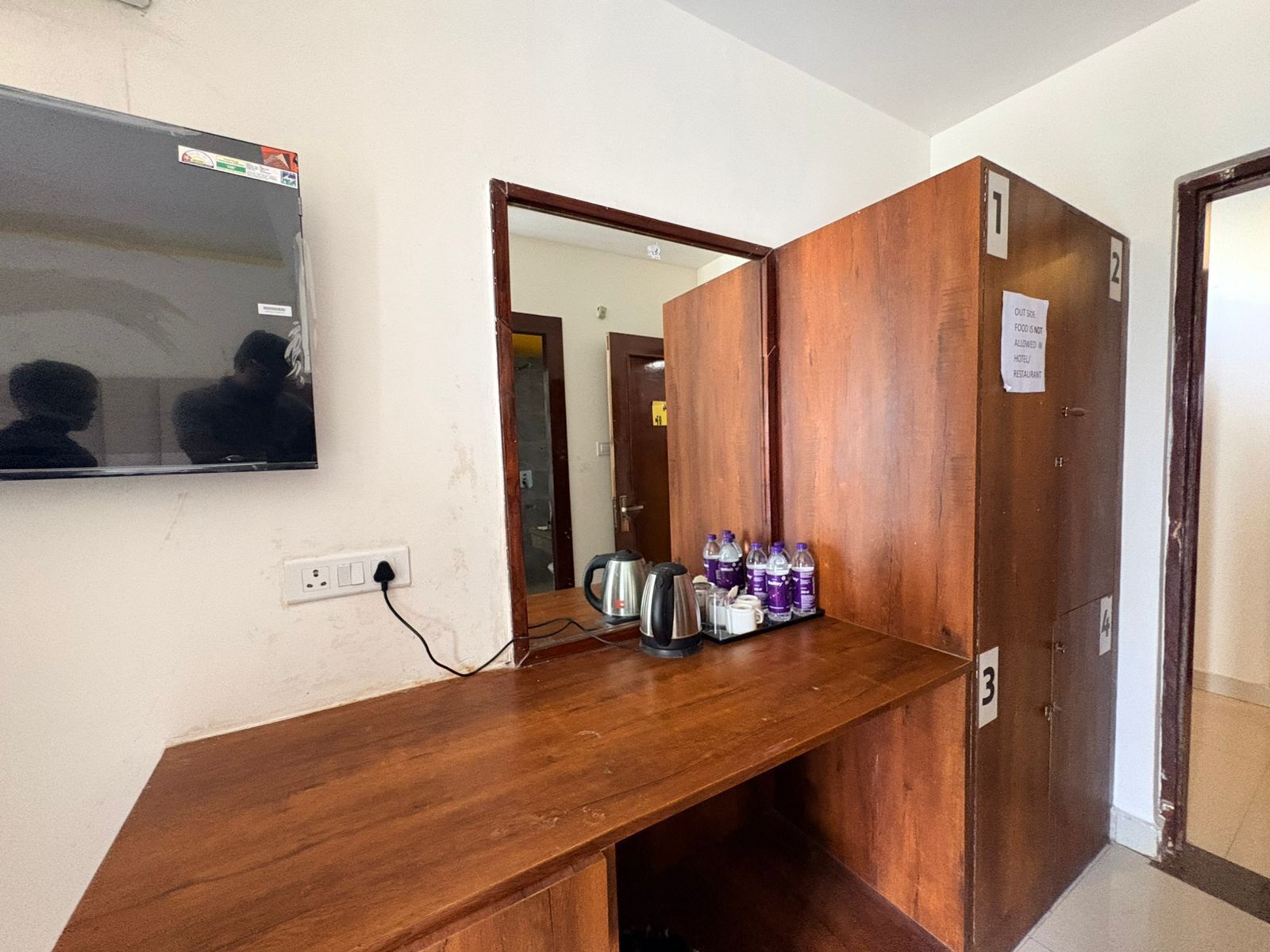 Una camera d'albergo con una scrivania in legno, una televisione fissata al muro e una porta con il simbolo del numero.