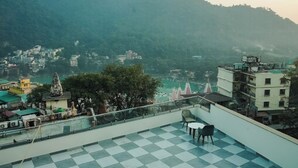 Terraço com chão xadrez, uma mesa e duas cadeiras. Ao fundo, vista de um vale com edifícios e uma colina.