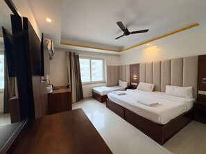Habitación de hotel con una cama grande, un escritorio, una silla, un ventilador de techo y una ventana con cortinas.