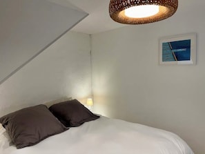 A bedroom with a bed, two pillows, a wall-mounted picture, and a hanging light fixture. - Panier Duplex — Terrace with Panoramic View of the Sea and the Rooftops of Marseille (Marseille)