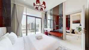 Una moderna camera d'hotel con un letto grande, un balcone affacciato sulla città, una parete di accento rosso e un'ampia finestra.