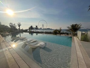 A clear swimming pool with lounge chairs, a Ferris wheel in the background, and a sunny sky. - Upgraded 1 Bedroom l JBR Beach l Private Beach (Dubai)