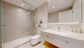 A modern bathroom with a glass-enclosed shower, a white toilet, and a large mirror above a white sink with toiletries. - Upgraded 1 Bedroom l JBR Beach l Private Beach (Dubai)