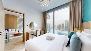 Ett modernt hotellrum med en stor säng, ett skrivbord, en stol, en rund spegel och utsikt över stadsbilden.