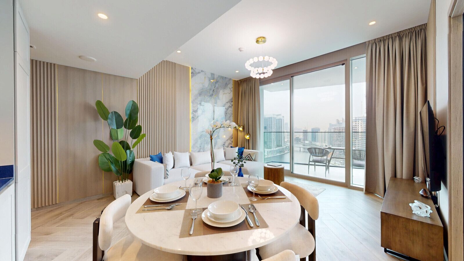 A modern dining area with a round table set for four, a sofa, and a large window with a city view.