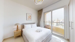 A hotel room with a bed, a nightstand, a lamp, a framed picture, and a view of a cityscape through a large window. - Peaceful Studio l City Skyline View l IMPZ (Dubai)