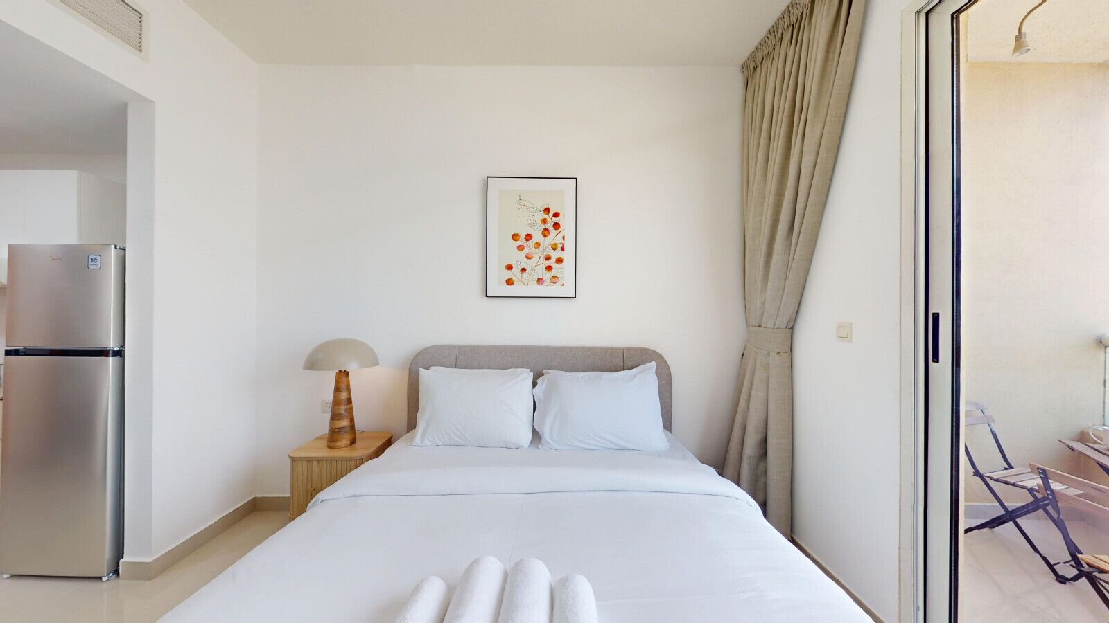 Une chambre d’hôtel avec un lit, une table de chevet, une lampe, un réfrigérateur et une fenêtre avec des rideaux.