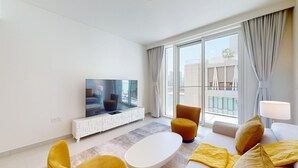Ein modernes Wohnzimmer mit Flachbildfernseher, weißem Konsolentisch, Sofa und Hocker.