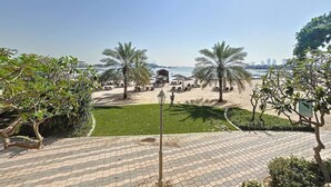 A paved pathway leading to a beach area with palm trees and a view of the city skyline. - Chic 2 Bed l Sea Views l Palm Jumeirah Retreat (Palm Jumeirah)