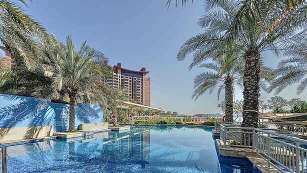 A swimming pool with clear blue water, surrounded by palm trees and a modern building in the background. - Chic 2 Bed l Sea Views l Palm Jumeirah Retreat (Palm Jumeirah)