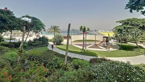 A landscaped area with a playground, palm trees, and a view of the sea. - Chic 2 Bed l Sea Views l Palm Jumeirah Retreat (Palm Jumeirah)
