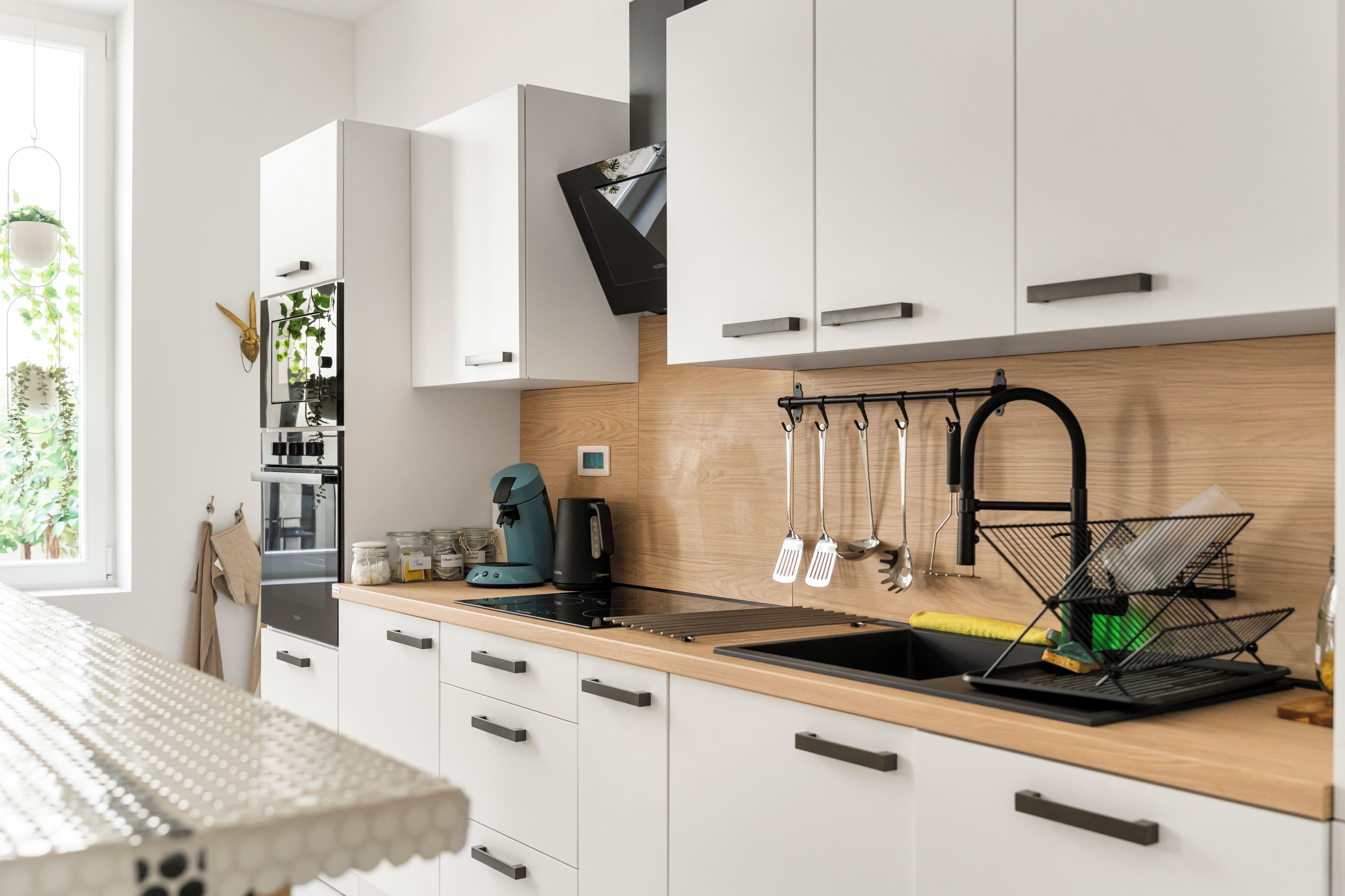 A modern kitchen with white cabinets, a wooden countertop, and various kitchen appliances.