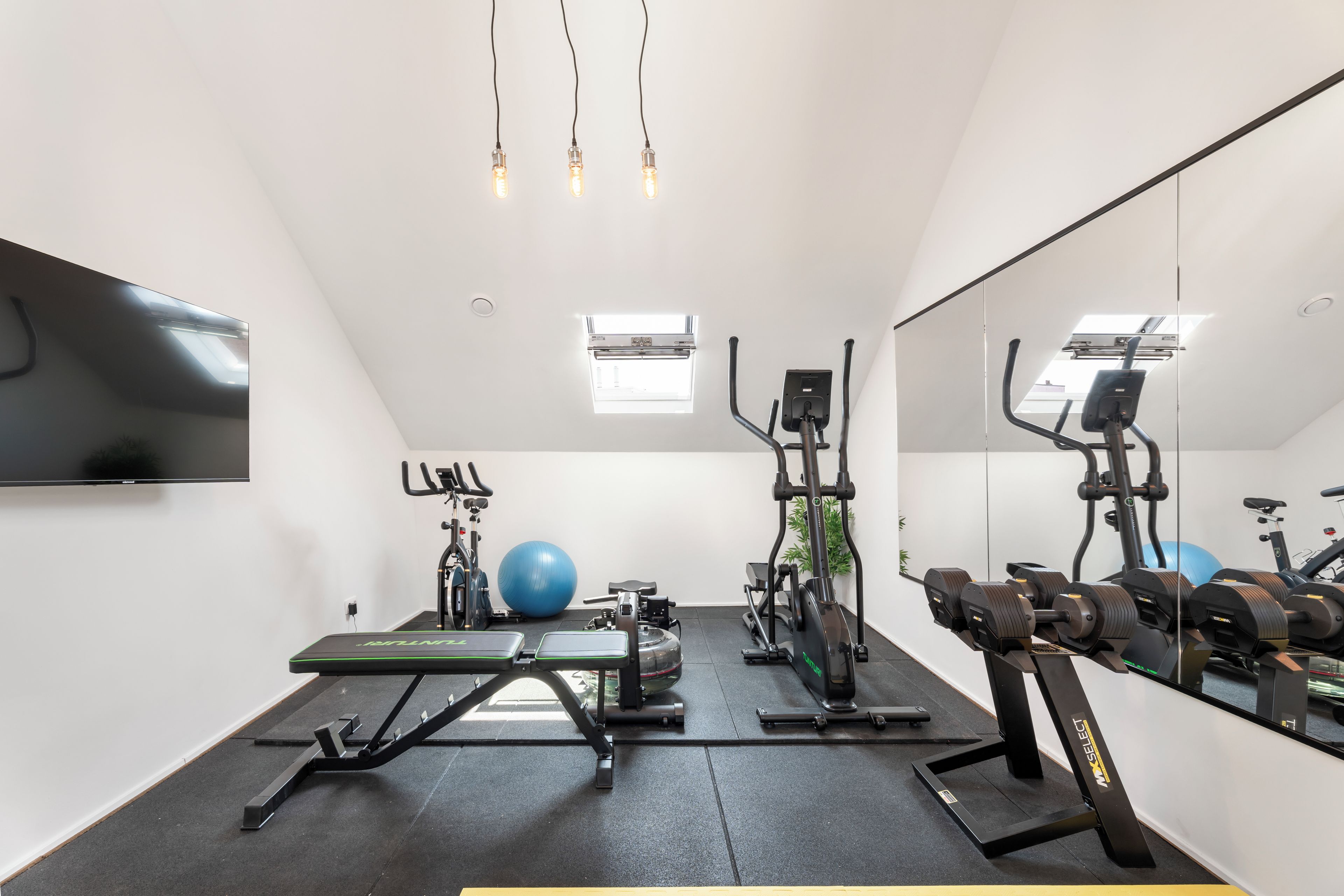 Ein modernes Fitnessstudio mit Trainingsgeräten, einem großen Spiegel und einem Fernseher an der Wand.