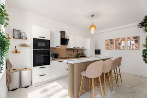 A modern kitchen with white cabinetry, a black microwave, and a wooden island with bar stools. - Vandenbranden Suites (Brussels)