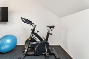 A stationary exercise bike with a blue exercise ball beside it, in a room with white walls and a black floor. - Vandenbranden Suites (Brussels)