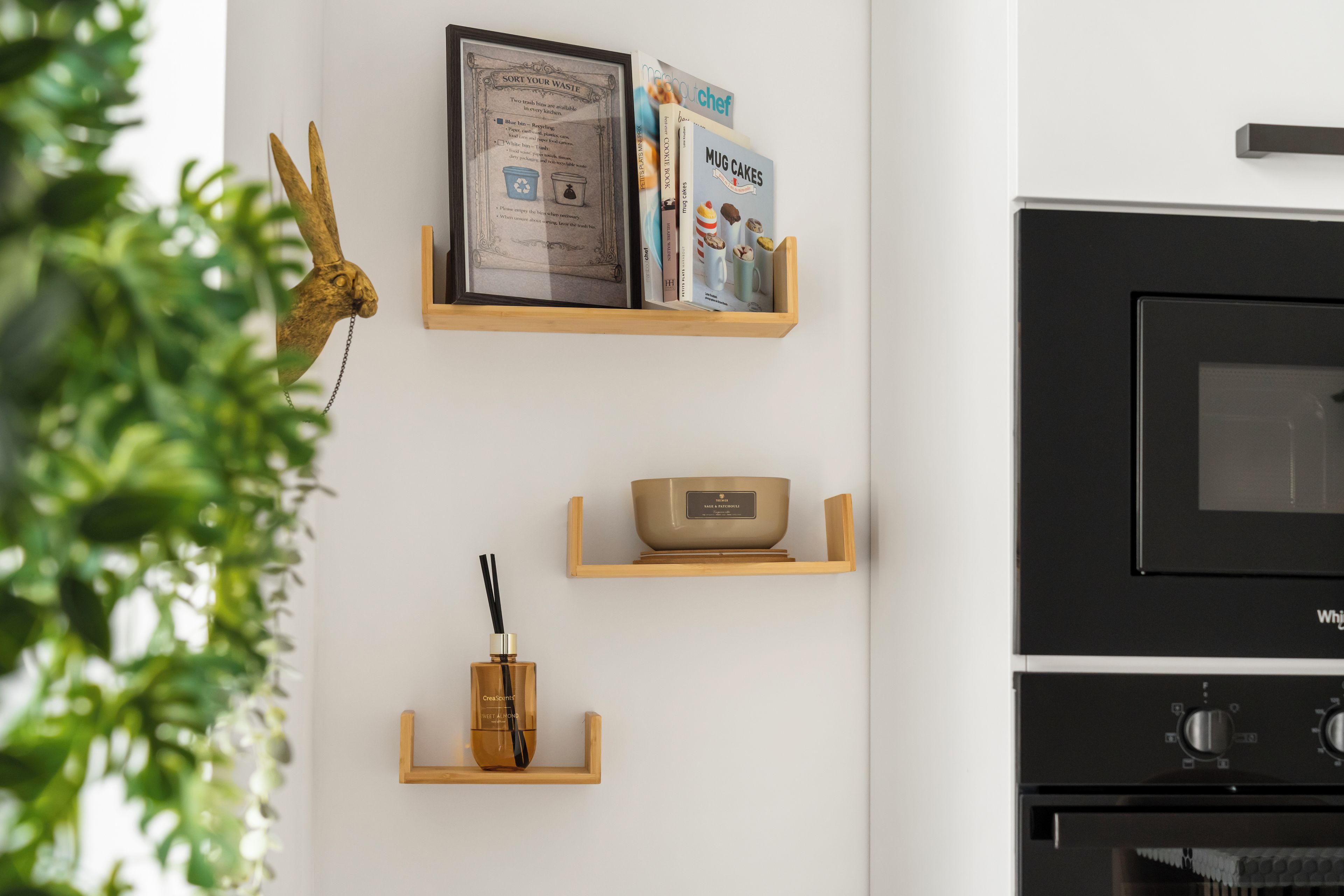 A kitchen with a black oven, a wooden shelf with a framed sign, and a plant.