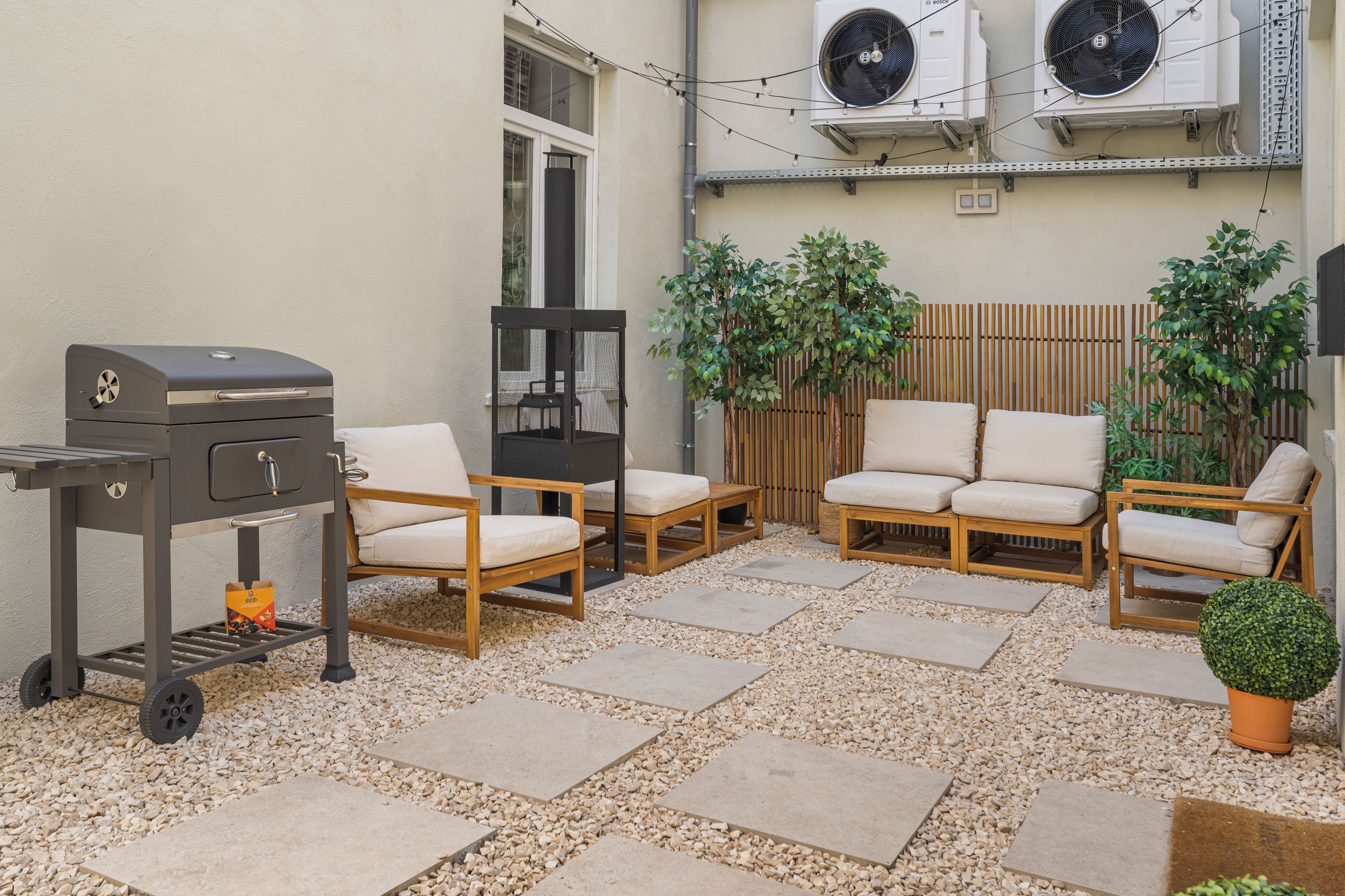 Une terrasse extérieure avec un barbecue, un espace salon et des plantes en pot.