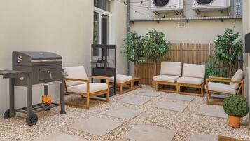 Une terrasse extérieure avec un barbecue, un espace salon et des plantes en pot.