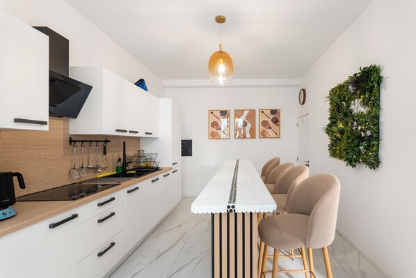 A modern kitchen with white cabinetry, a wooden countertop, and a dining area with a long table and chairs. - Vandenbranden Suites (Brussels)