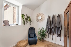 A modern living space with a black leather chair, a woven pouf, a potted plant, and a wall-mounted mirror. - Vandenbranden Suites (Brussels)