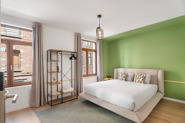 A bedroom with a bed, a shelf unit, a window, and a green wall. - Vandenbranden Suites (Brussels)