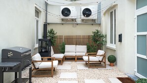 An outdoor patio with a grill, seating area, and air conditioning units.