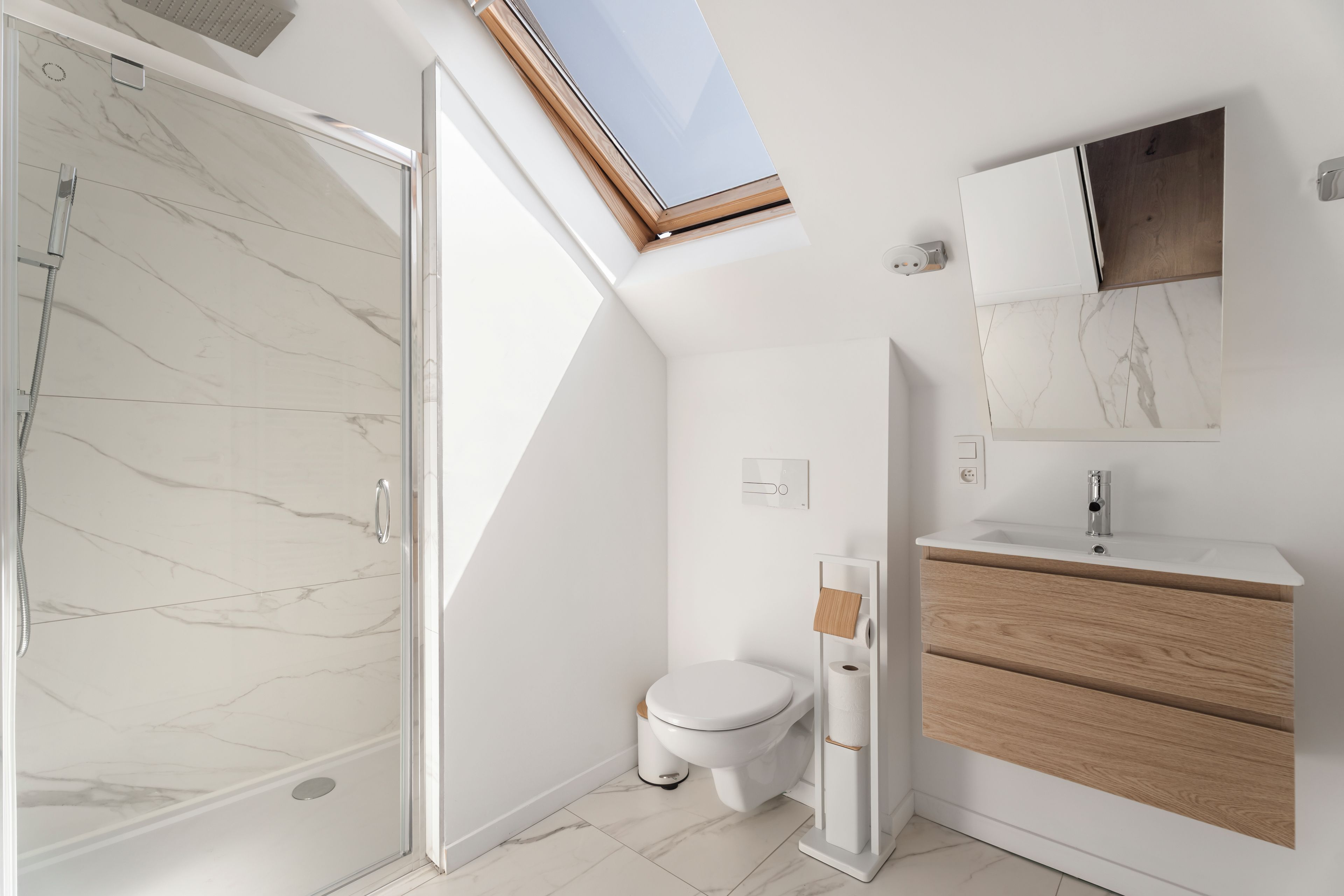 Un baño moderno con cabina de ducha de vidrio, inodoro y tocador con espejo y lavamanos.