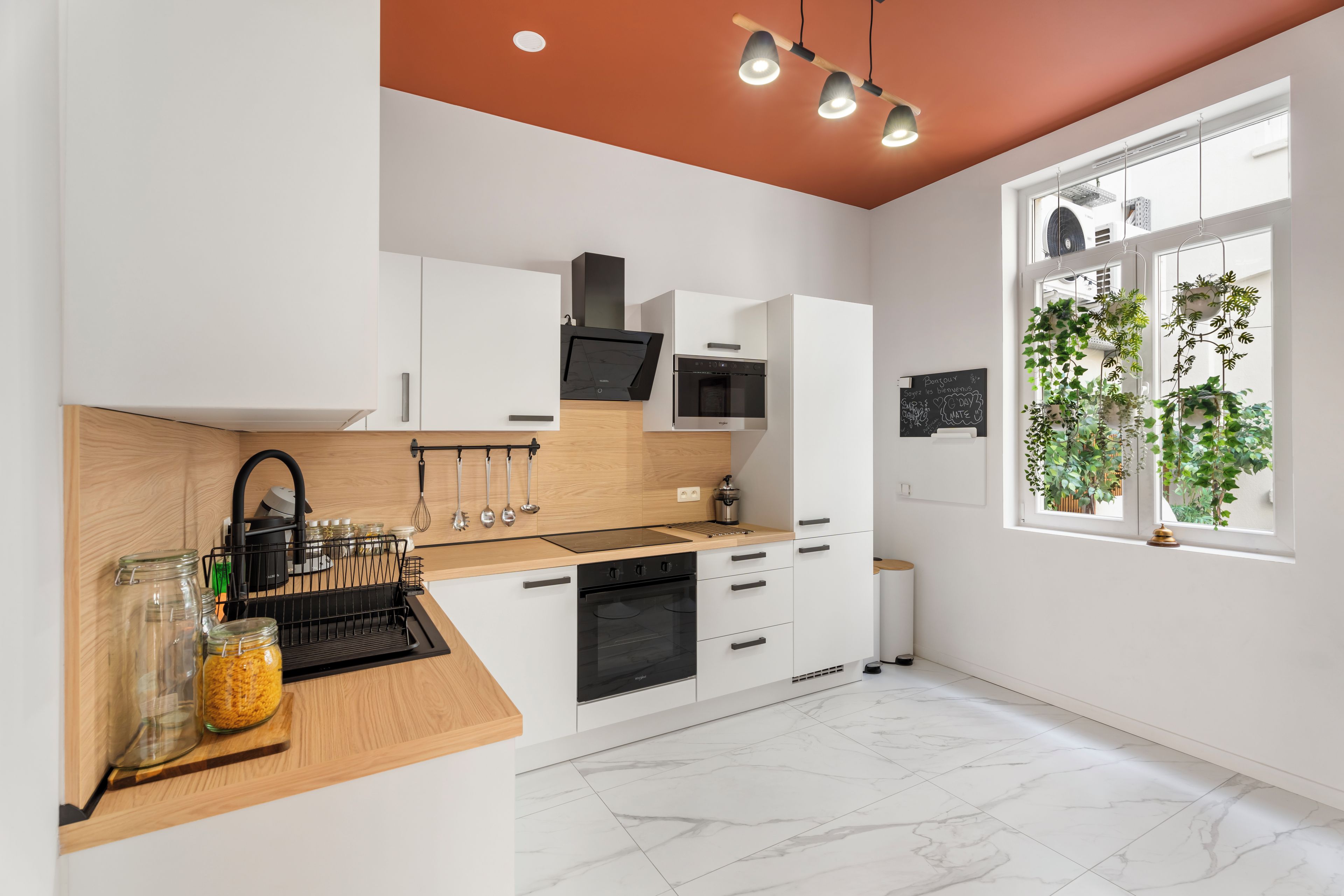 A modern kitchen with white cabinetry, a wooden countertop, and a view of greenery through a window.