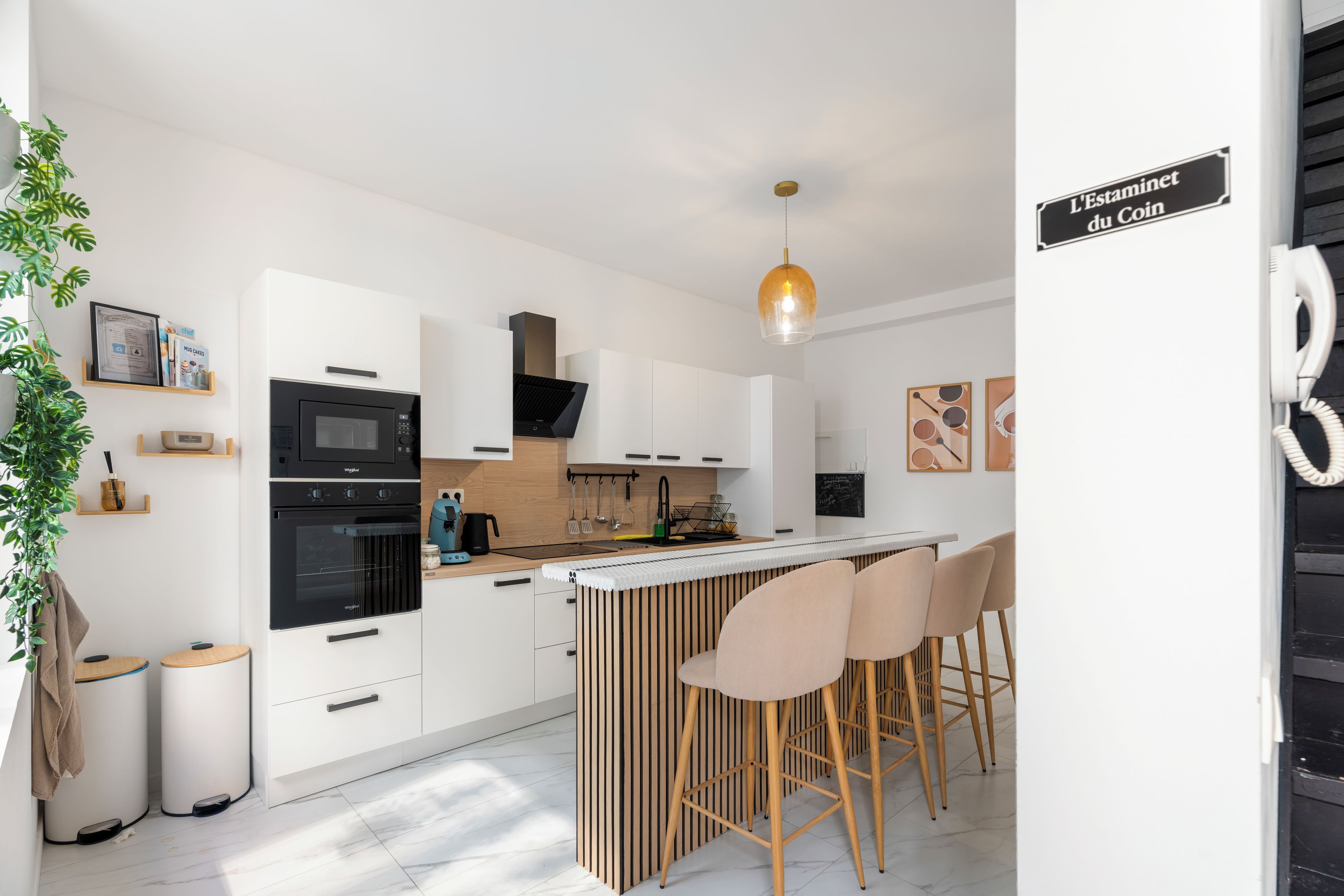 Une cuisine moderne avec des meubles blancs, un four encastré, un four à micro-ondes et un luminaire suspendu.