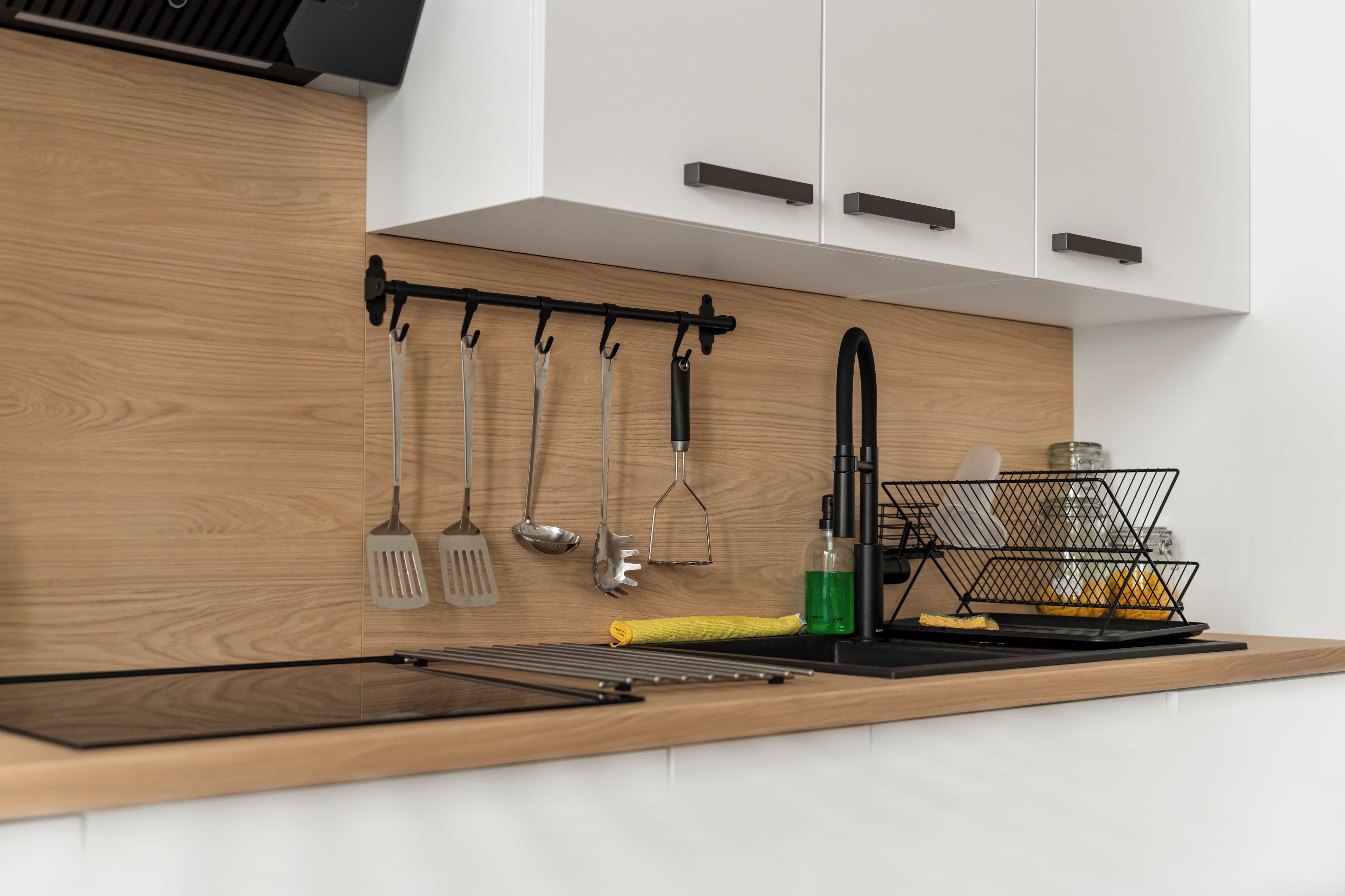 Een moderne keuken met houten kastjes, een zwart aanrechtblad en diverse keukengerei dat aan een rek hangt.
