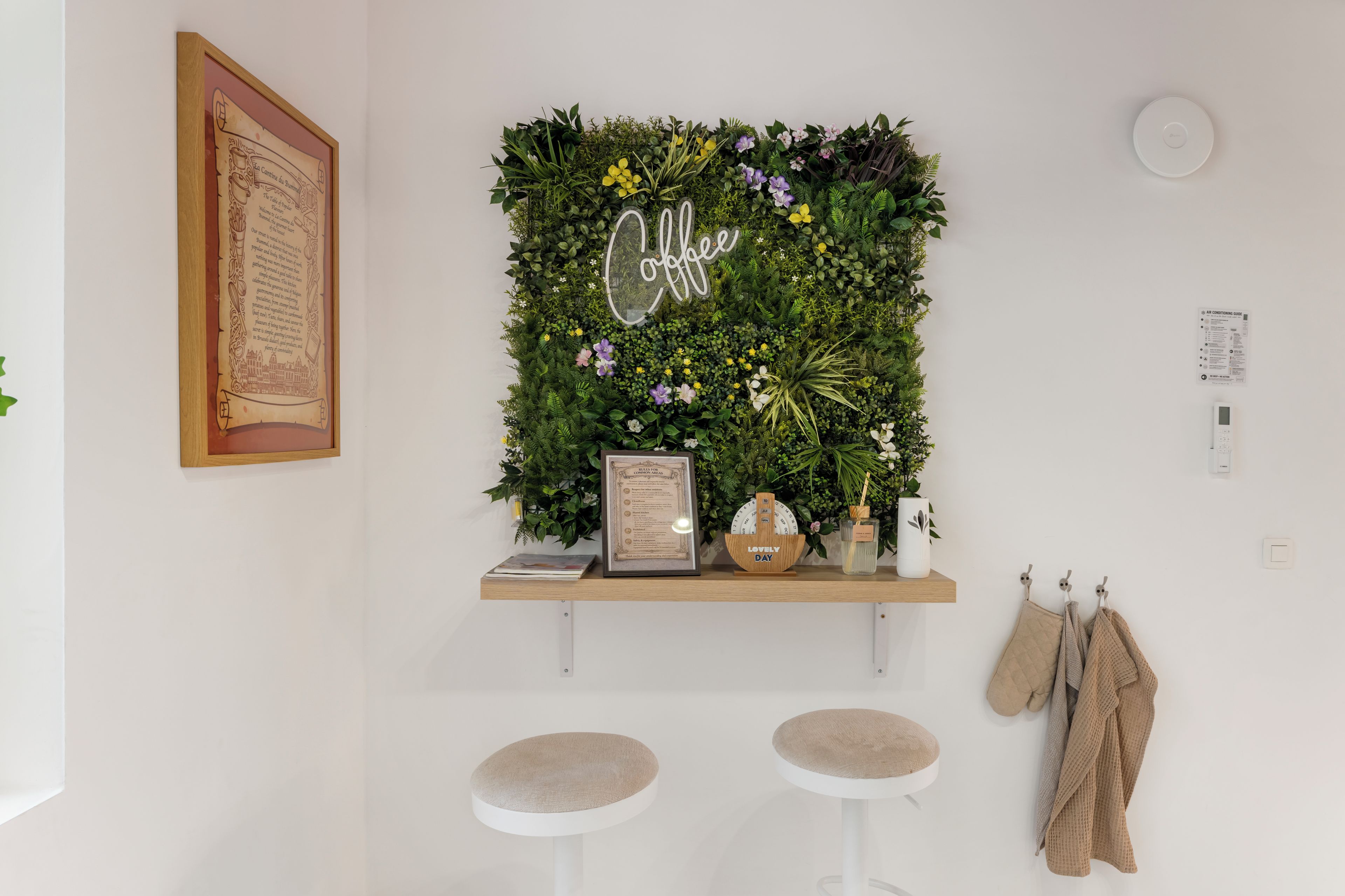 Un mur agrémenté d’un jardin vertical, un menu encadré et une petite étagère avec une horloge et un vase.