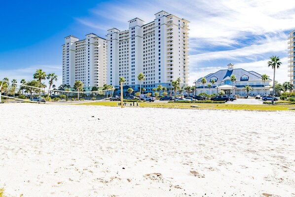 A beachfront hotel with multiple high-rise buildings, a sandy beach, and a parking area with cars.