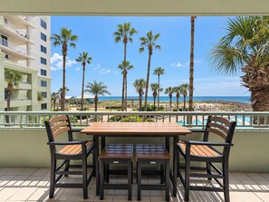 Un balcon avec une table et des chaises en bois, donnant sur une plage bordée de palmiers et offrant une vue sur un ciel dégagé.
