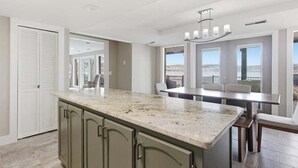 A modern kitchen with a granite countertop, a dining area with a table and chairs, and a view through large windows. - Outdoor Dream Lakefront Home w/ Private Dock, 2 Slips & Kayak (Sunrise Beach)
