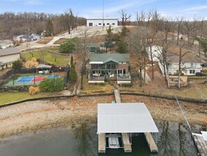 A lakeside property with a dock, a tennis court, and a building with a green roof.