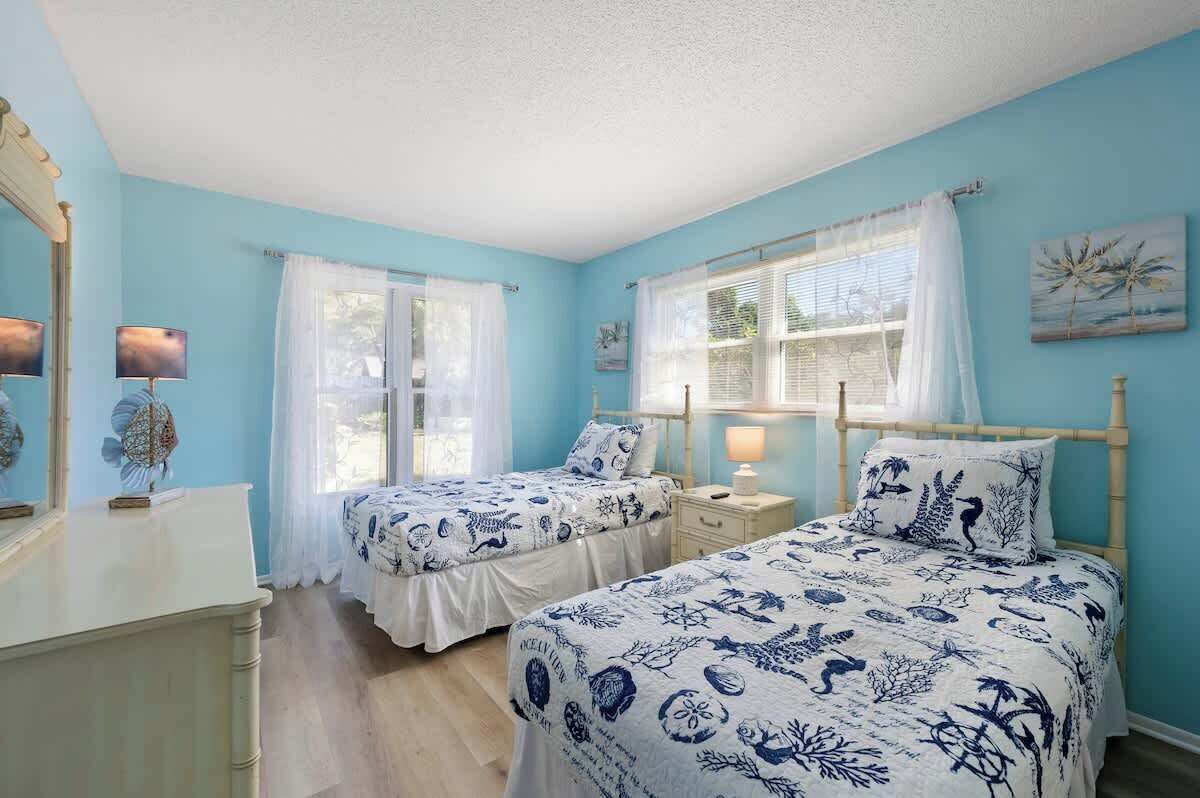 A bedroom with two beds, a dresser, and a window with curtains.