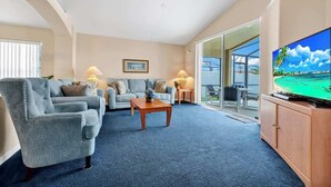 Una sala de estar con sofá, sillón, mesa de centro y televisor.