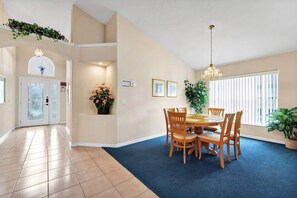 A dining area with a round table and chairs, a potted plant, and a window with blinds. - Modern 4BR Family Home w/ Pool - 15 min Disney (Davenport)