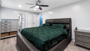 Una camera da letto con un letto, un ventilatore a soffitto, una cassettiera e un comodino.