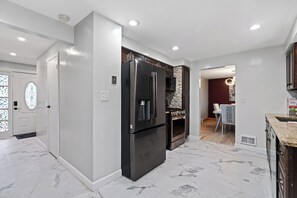 A modern kitchen with a stainless steel refrigerator, a built-in oven, and marble flooring.
