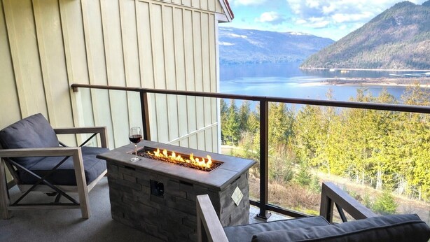 Un balcone con un braciere in pietra, due poltrone imbottite e vista su un lago e montagne.