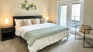 Una camera da letto con un letto, due comodini, un tavolino, un divano, un elemento decorativo a parete e una porta scorrevole in vetro.